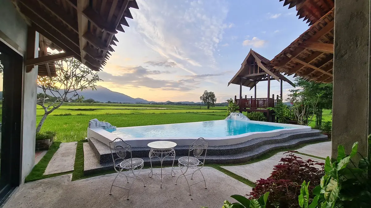 Infinity pool and wooden gazebo at sunset with padi fields stretching to the mountains